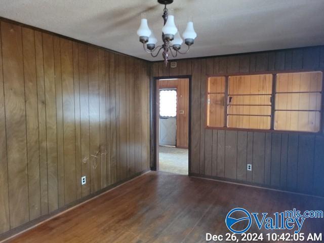 spare room featuring dark hardwood / wood-style flooring, an inviting chandelier, and wood walls