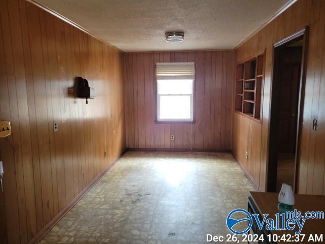 unfurnished room with crown molding, a textured ceiling, and wooden walls