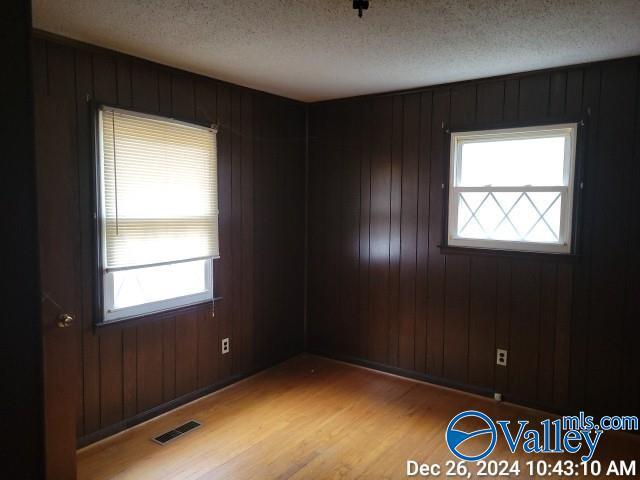 empty room featuring wood walls, a textured ceiling, and light wood-type flooring