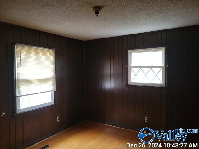 spare room with a textured ceiling, light hardwood / wood-style flooring, and wooden walls