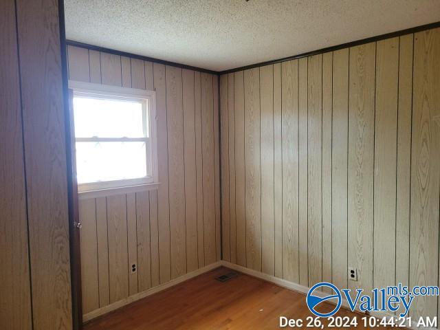 unfurnished room with hardwood / wood-style floors, a textured ceiling, and wood walls