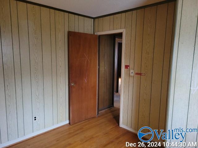 unfurnished bedroom featuring wood walls, ornamental molding, and light wood-type flooring