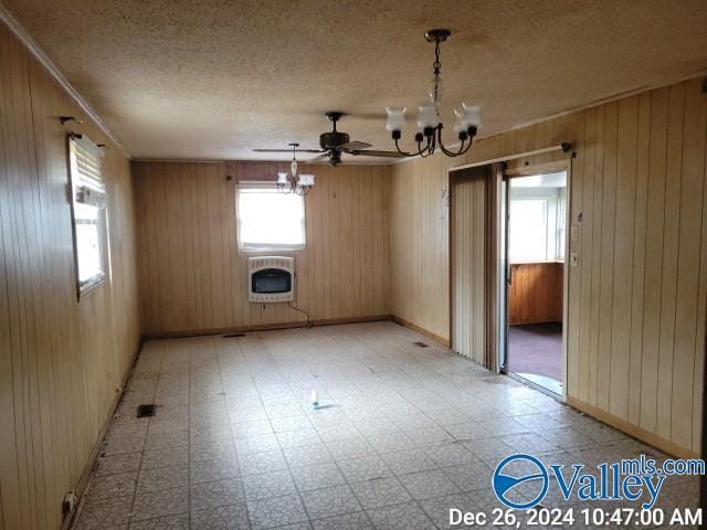 unfurnished room featuring a textured ceiling, heating unit, wood walls, and ceiling fan with notable chandelier