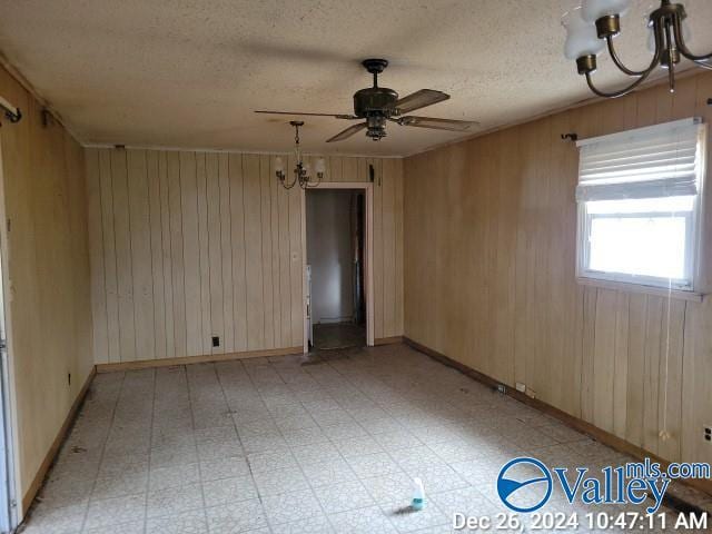 unfurnished room featuring ceiling fan with notable chandelier, wood walls, and a textured ceiling