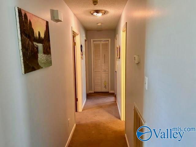 hallway with a textured ceiling, baseboards, and light colored carpet