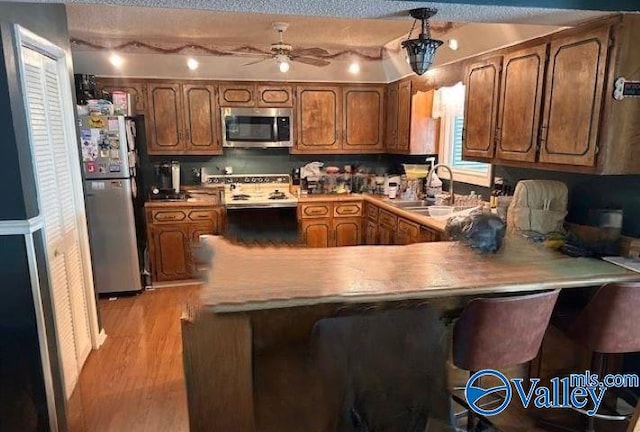 kitchen featuring a peninsula, a sink, light wood-style floors, appliances with stainless steel finishes, and brown cabinets