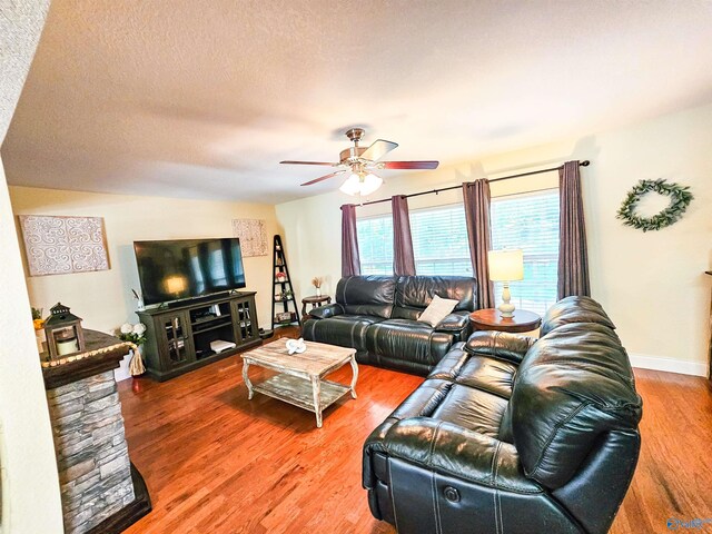 living room with a stone fireplace, a textured ceiling, hardwood / wood-style floors, and ceiling fan