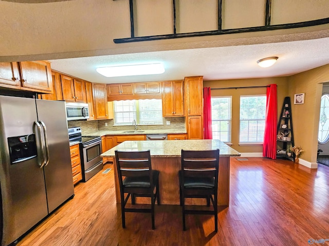 kitchen with sink, a breakfast bar area, appliances with stainless steel finishes, tasteful backsplash, and a kitchen island