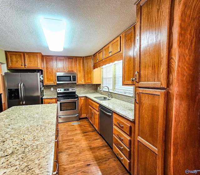 kitchen with sink, tasteful backsplash, light hardwood / wood-style flooring, appliances with stainless steel finishes, and light stone countertops