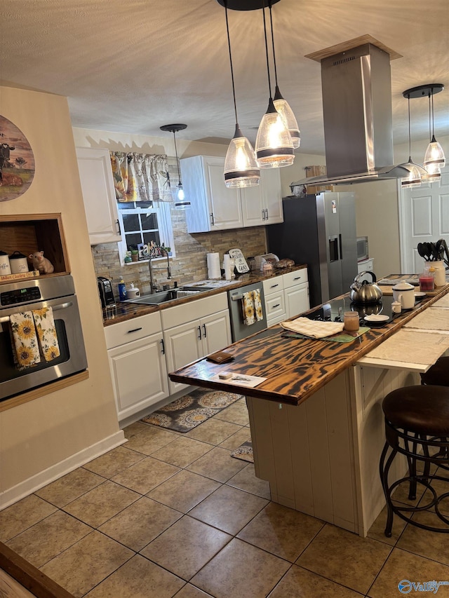 kitchen with appliances with stainless steel finishes, island range hood, butcher block counters, white cabinets, and a kitchen breakfast bar