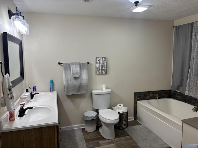 bathroom with wood-type flooring, a tub to relax in, vanity, toilet, and a textured ceiling