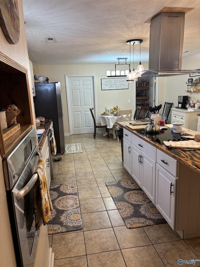 kitchen featuring butcher block counters, hanging light fixtures, light tile patterned floors, appliances with stainless steel finishes, and white cabinets