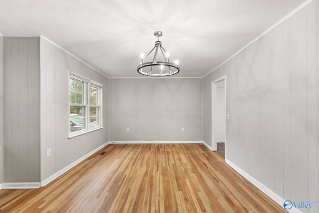 unfurnished dining area with crown molding, light hardwood / wood-style floors, wood walls, and an inviting chandelier