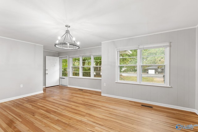 empty room featuring a notable chandelier, light hardwood / wood-style floors, crown molding, and wooden walls