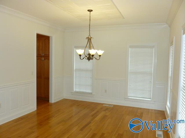 unfurnished dining area with light wood-style flooring, ornamental molding, a chandelier, and visible vents