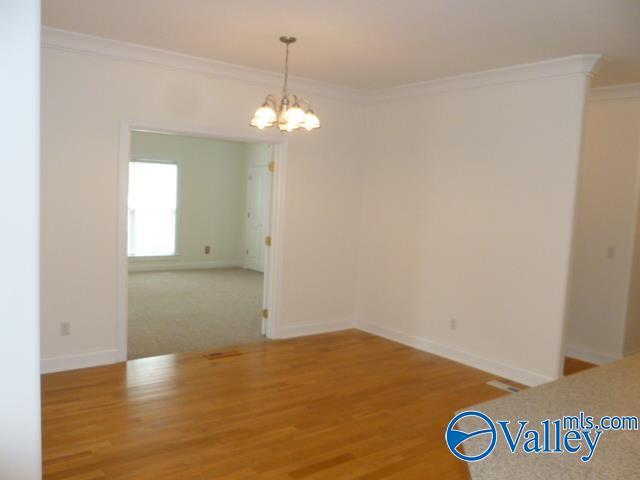 unfurnished dining area with an inviting chandelier, crown molding, and wood finished floors
