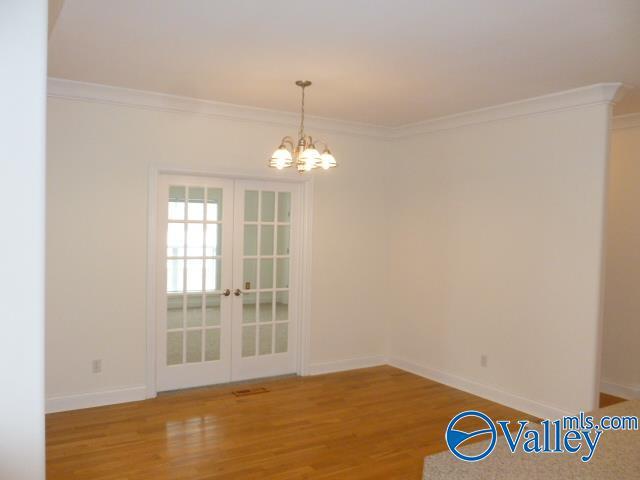 unfurnished dining area featuring french doors, ornamental molding, baseboards, a chandelier, and wood finished floors