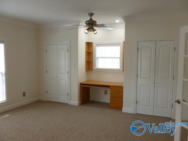 unfurnished bedroom with baseboards, two closets, crown molding, and light carpet