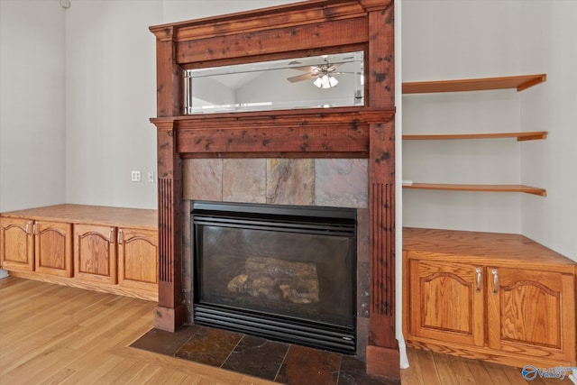 details featuring wood finished floors, a tiled fireplace, and a ceiling fan