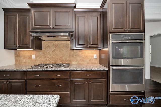 kitchen with dark brown cabinetry, decorative backsplash, stainless steel appliances, and wall chimney exhaust hood