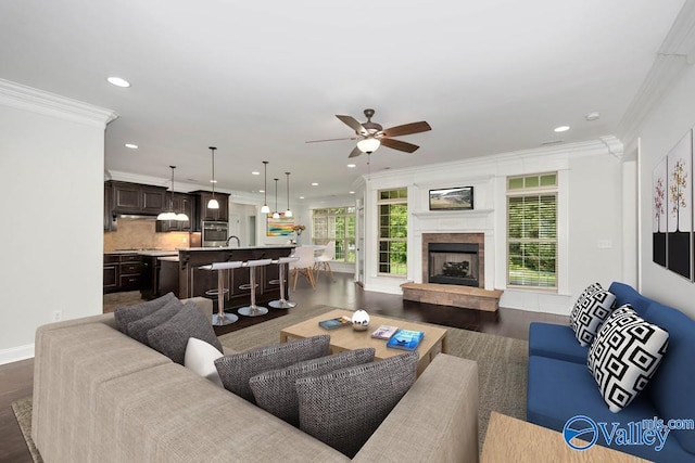 living room featuring ceiling fan, a tiled fireplace, dark hardwood / wood-style flooring, and ornamental molding