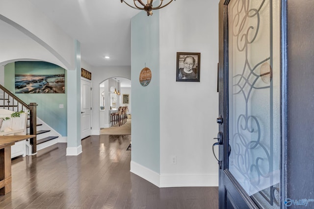 foyer entrance featuring dark wood-style floors, arched walkways, baseboards, and stairs