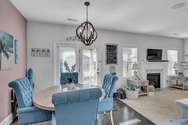 dining area with a chandelier, wood finished floors, visible vents, and a premium fireplace