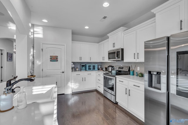 kitchen with arched walkways, stainless steel appliances, light countertops, decorative backsplash, and dark wood-type flooring