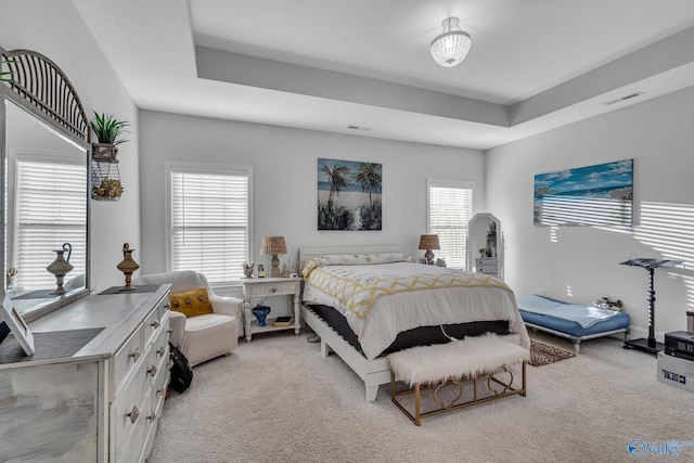 bedroom featuring a tray ceiling, light colored carpet, and visible vents