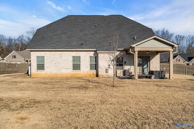 rear view of house with brick siding, a patio, a shingled roof, a lawn, and a fenced backyard