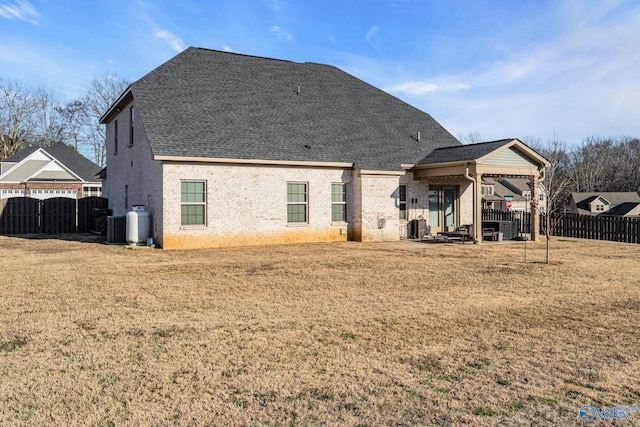 rear view of house with central AC unit, a lawn, a shingled roof, and brick siding