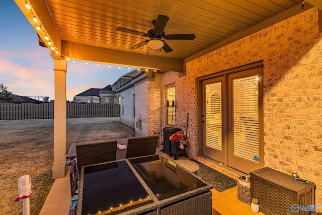 patio terrace at dusk featuring a ceiling fan and fence