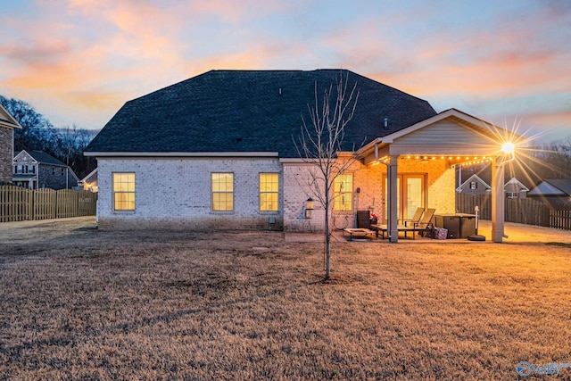 back of property at dusk featuring a patio, brick siding, a lawn, and fence