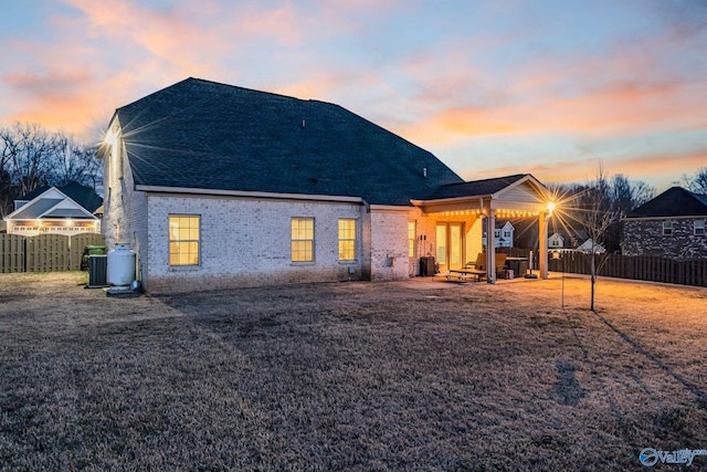 back of property at dusk with a patio area, a fenced backyard, a lawn, and brick siding