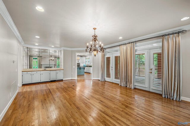 unfurnished living room with light wood-type flooring, a notable chandelier, and ornamental molding