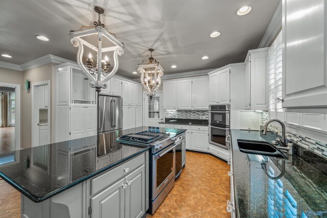 kitchen with dark stone countertops, stainless steel appliances, a chandelier, white cabinetry, and sink