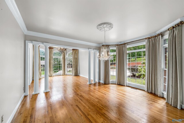 unfurnished room with crown molding, light hardwood / wood-style floors, a chandelier, and decorative columns