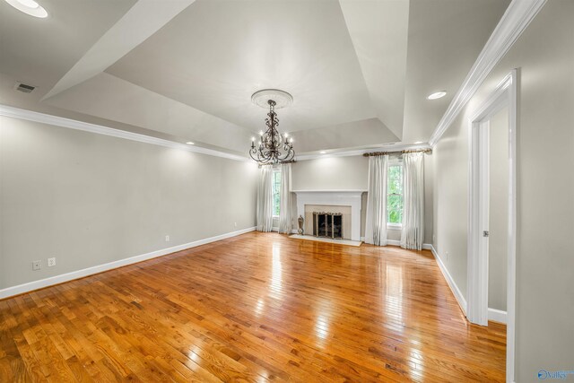 unfurnished living room with a tray ceiling, light wood-type flooring, ornamental molding, and a healthy amount of sunlight