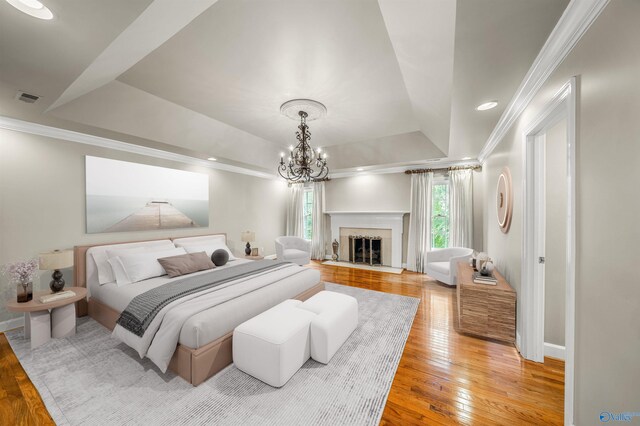 bedroom featuring a raised ceiling, light wood-type flooring, a premium fireplace, and multiple windows