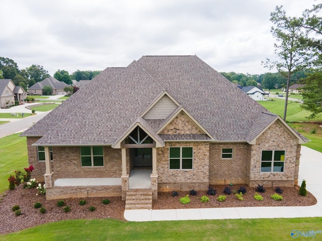 craftsman house with a shingled roof, a front yard, and brick siding