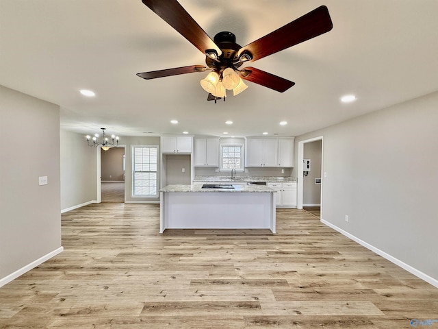 kitchen with a kitchen island, ceiling fan with notable chandelier, white cabinets, light hardwood / wood-style floors, and light stone countertops