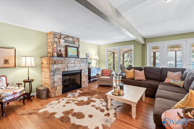 living room with french doors, beam ceiling, a stone fireplace, and light wood-type flooring