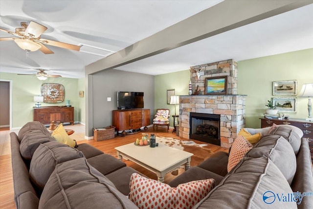 living room with light wood-type flooring, ceiling fan, a stone fireplace, and beamed ceiling