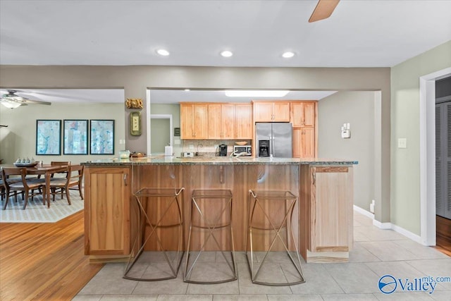 kitchen featuring light tile patterned floors, backsplash, stainless steel fridge with ice dispenser, and stone countertops