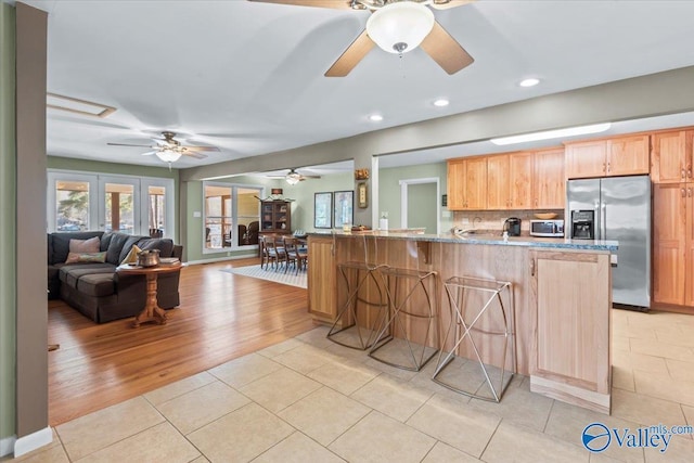 kitchen featuring kitchen peninsula, stainless steel appliances, light tile patterned flooring, light stone countertops, and a breakfast bar