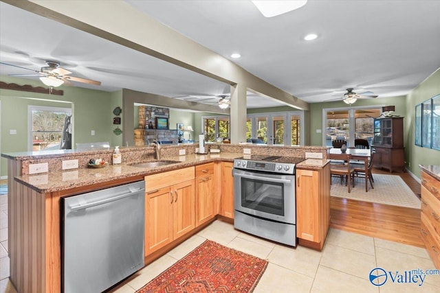 kitchen with light tile patterned floors, kitchen peninsula, stainless steel appliances, light stone countertops, and sink