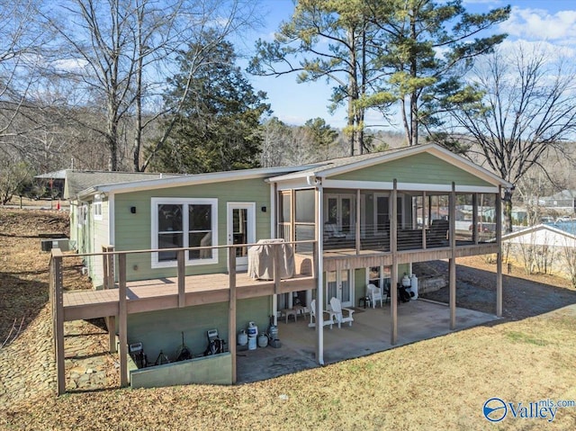 rear view of property featuring a wooden deck, a sunroom, and a patio