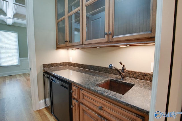 kitchen with brown cabinets, light wood-style floors, glass insert cabinets, a sink, and dishwasher