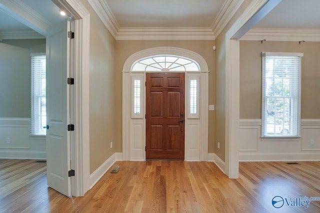 entrance foyer featuring visible vents, a decorative wall, light wood-style flooring, ornamental molding, and wainscoting