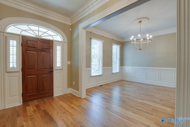 entrance foyer with ornamental molding, a chandelier, wainscoting, and light wood finished floors